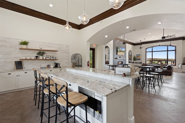 bar with ceiling fan, arched walkways, stainless steel microwave, decorative backsplash, and ornamental molding