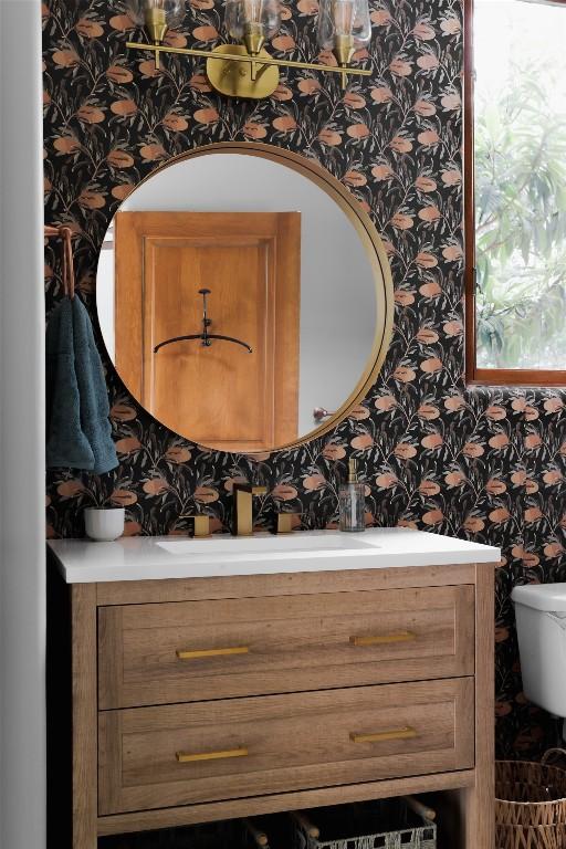 half bath featuring vanity, toilet, and wallpapered walls