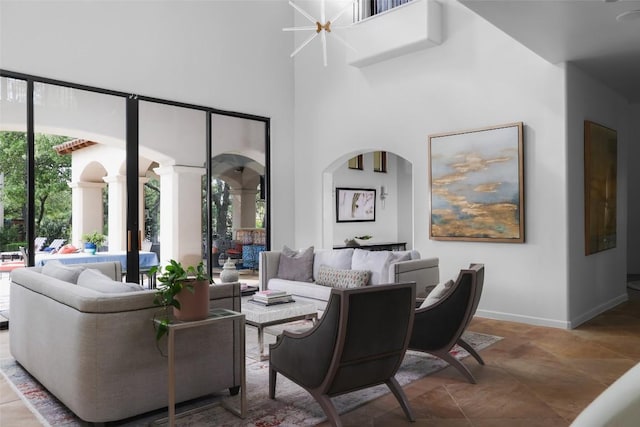 living room with baseboards, arched walkways, ornate columns, and a high ceiling