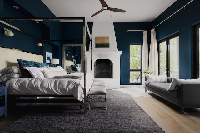 bedroom featuring a ceiling fan, wood finished floors, and a fireplace