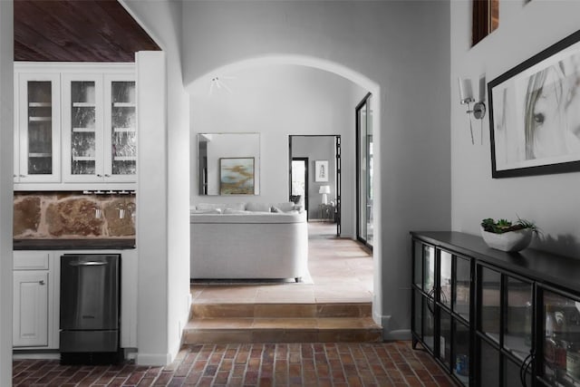 corridor featuring arched walkways, brick floor, and a high ceiling