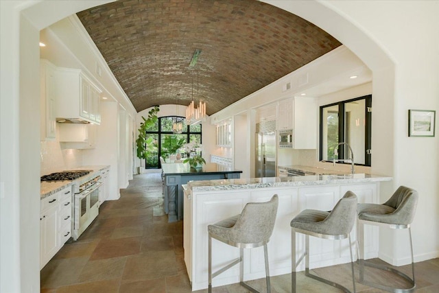 201 Costa Bella Dr, Austin, TX 78734 - kitchen featuring built in appliances, vaulted ceiling, white cabinets, a breakfast bar, and brick ceiling