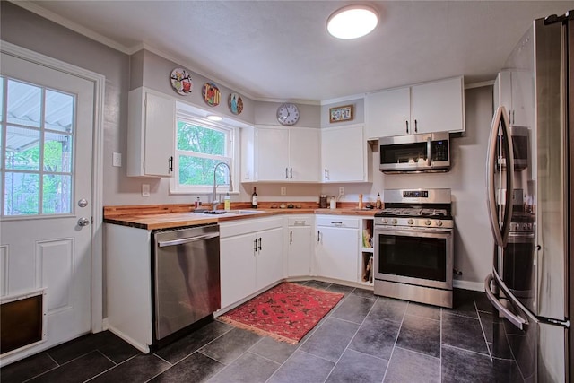 kitchen featuring white cabinets, a sink, stainless steel appliances, ornamental molding, and butcher block counters