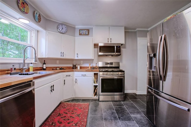 kitchen with a sink, appliances with stainless steel finishes, baseboards, and white cabinetry