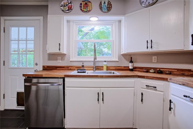 kitchen with a sink, dishwasher, butcher block countertops, white cabinetry, and dark tile patterned flooring