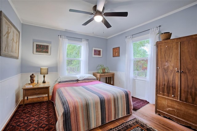 bedroom featuring wood finished floors, multiple windows, and a wainscoted wall