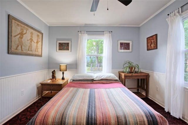 carpeted bedroom with crown molding, multiple windows, a ceiling fan, and wainscoting