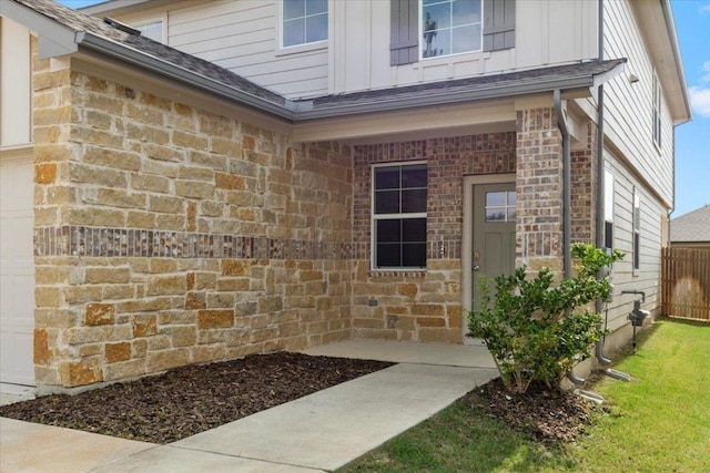 doorway to property featuring board and batten siding, brick siding, fence, and a garage