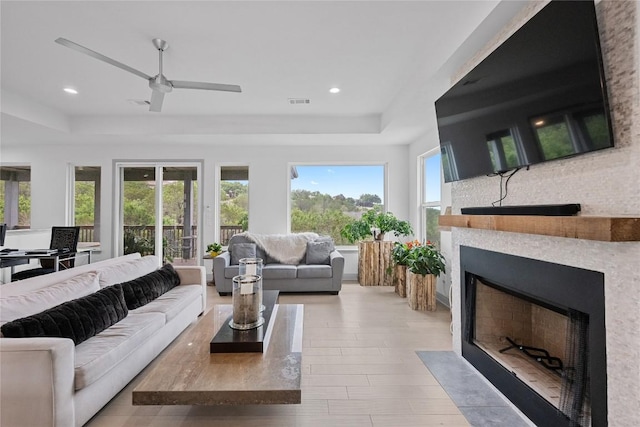 living room with a fireplace with flush hearth, a raised ceiling, and a healthy amount of sunlight