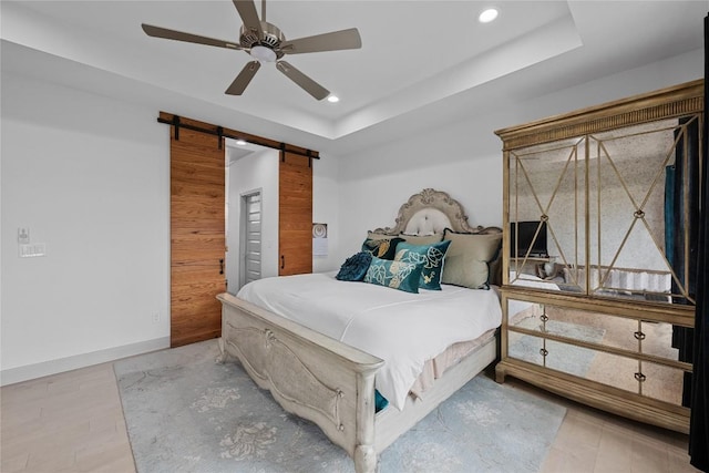 bedroom featuring a ceiling fan, a barn door, wood finished floors, a raised ceiling, and recessed lighting