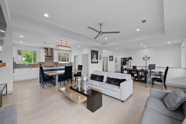 living area featuring a raised ceiling, light wood finished floors, recessed lighting, and visible vents