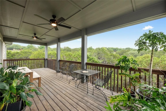 deck featuring outdoor dining area, ceiling fan, and a forest view