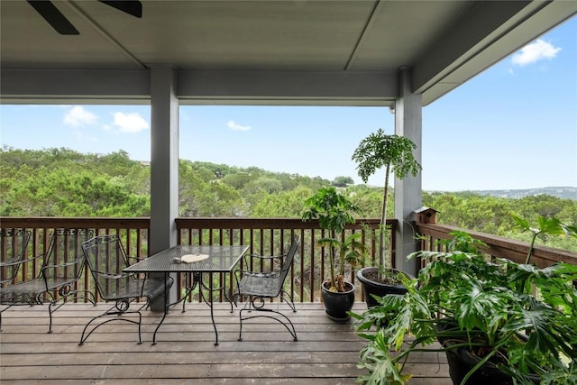 wooden deck featuring a ceiling fan, outdoor dining area, and a forest view