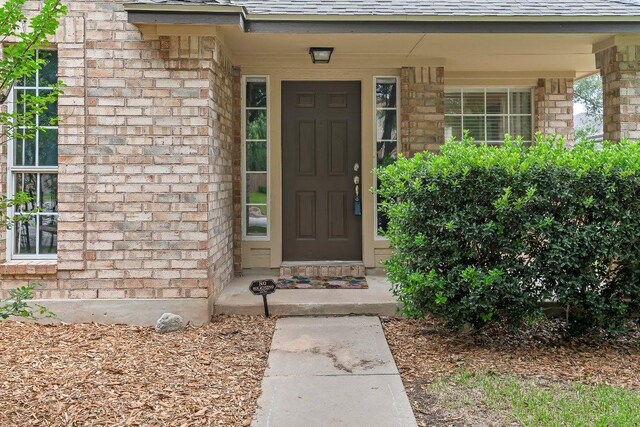 property entrance featuring roof with shingles, covered porch, and brick siding