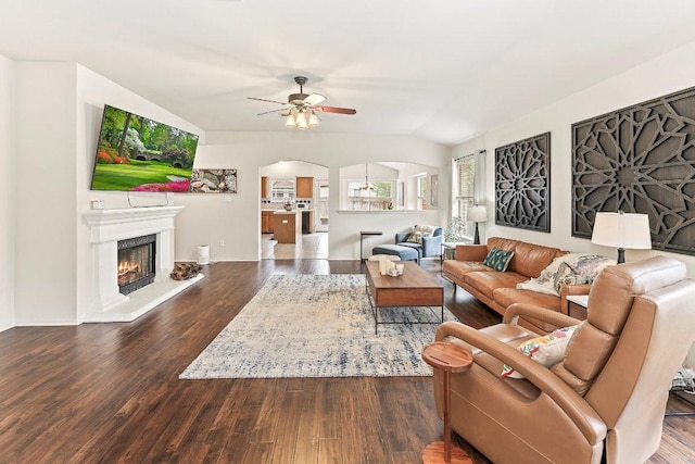 living room with arched walkways, a ceiling fan, wood finished floors, lofted ceiling, and a lit fireplace
