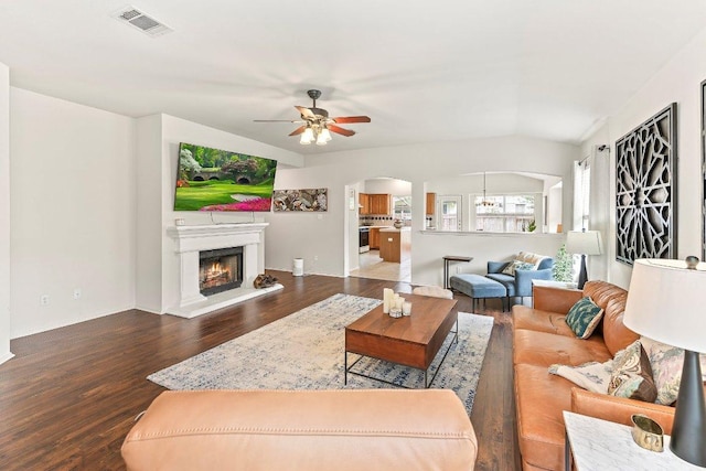 living room featuring visible vents, ceiling fan, a lit fireplace, dark wood-type flooring, and arched walkways