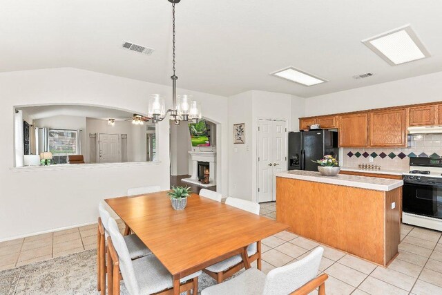 kitchen featuring black fridge with ice dispenser, visible vents, under cabinet range hood, range with gas cooktop, and light tile patterned floors