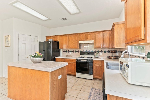 kitchen with range with gas stovetop, freestanding refrigerator, white microwave, under cabinet range hood, and light tile patterned floors
