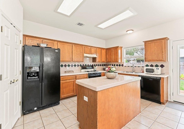 kitchen with backsplash, visible vents, a sink, black appliances, and under cabinet range hood