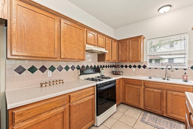 kitchen with backsplash, gas range, brown cabinets, a sink, and under cabinet range hood
