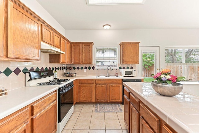 kitchen with white microwave, a sink, gas stove, tasteful backsplash, and under cabinet range hood