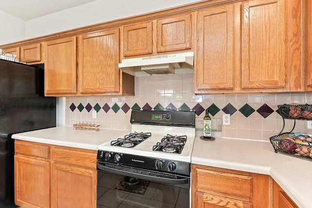kitchen featuring under cabinet range hood, gas range oven, freestanding refrigerator, and light countertops
