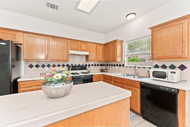 kitchen with visible vents, a sink, black appliances, tile counters, and under cabinet range hood