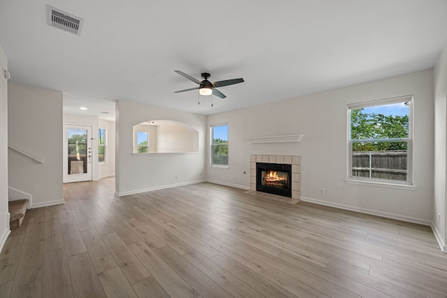 unfurnished living room featuring a tiled fireplace, a ceiling fan, wood finished floors, and visible vents
