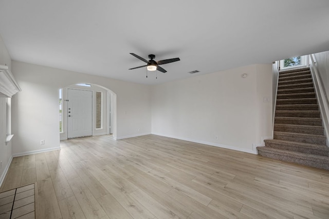 unfurnished living room with arched walkways, a ceiling fan, stairs, and visible vents