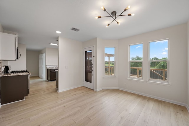 unfurnished living room featuring baseboards, an inviting chandelier, light wood finished floors, and visible vents