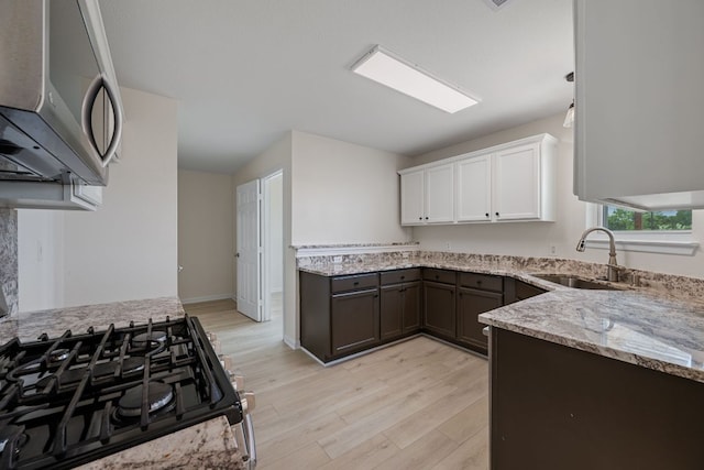 kitchen featuring stainless steel microwave, light stone counters, a sink, light wood finished floors, and gas stove