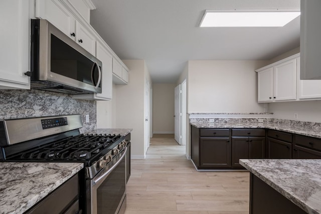 kitchen with appliances with stainless steel finishes, light wood-style flooring, backsplash, and white cabinetry