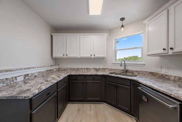 kitchen with stainless steel dishwasher, light stone countertops, white cabinets, a sink, and light wood finished floors