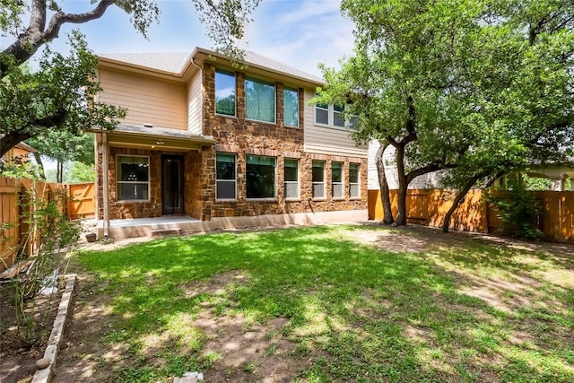 back of house featuring a lawn, covered porch, a fenced backyard, and stone siding