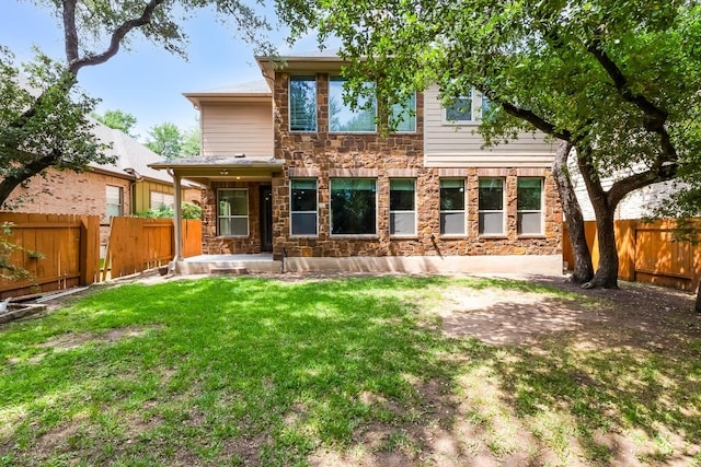 rear view of property featuring a fenced backyard, a yard, and stone siding