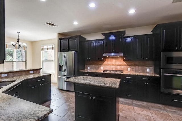 kitchen with dark cabinetry, stainless steel appliances, tasteful backsplash, under cabinet range hood, and visible vents