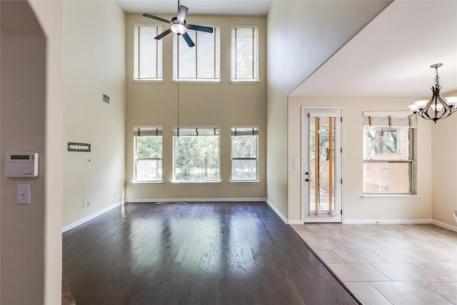 interior space with visible vents, a towering ceiling, wood finished floors, baseboards, and ceiling fan with notable chandelier