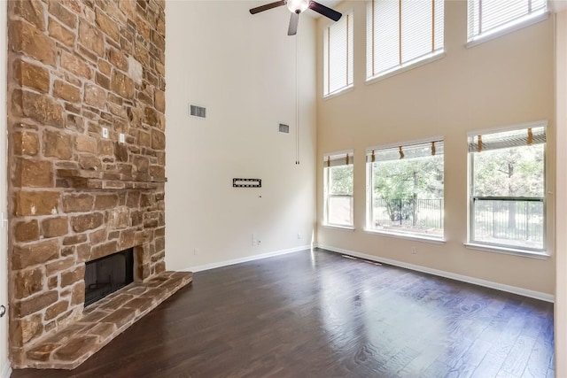 unfurnished living room with a ceiling fan, a towering ceiling, dark wood-style floors, and a fireplace