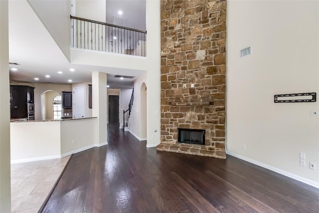 unfurnished living room featuring visible vents, arched walkways, a fireplace, wood finished floors, and a high ceiling
