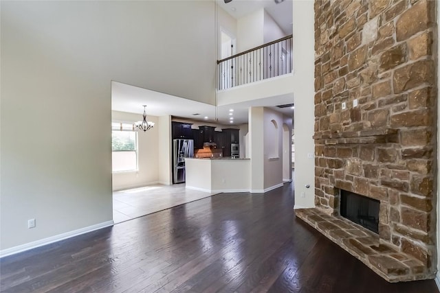 unfurnished living room featuring a stone fireplace, baseboards, a chandelier, and hardwood / wood-style flooring