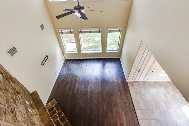 unfurnished living room featuring ceiling fan, baseboards, wood finished floors, a towering ceiling, and visible vents