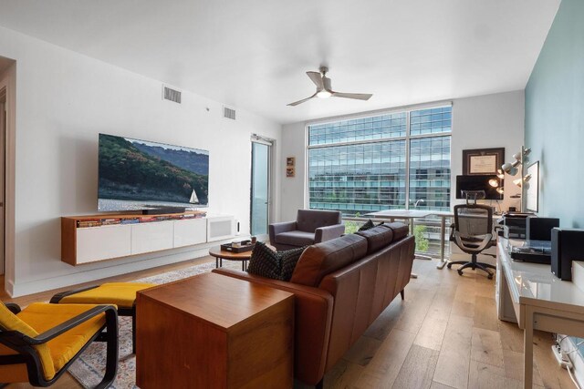 living room featuring ceiling fan, visible vents, expansive windows, and light wood-style floors