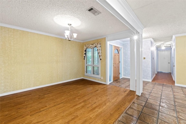 spare room with a notable chandelier, a textured ceiling, baseboards, visible vents, and ornamental molding