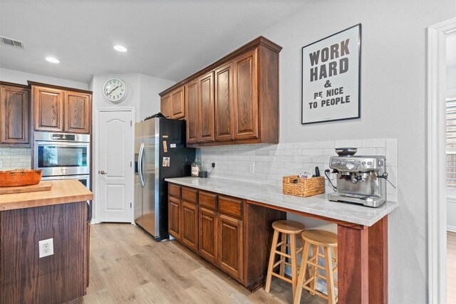 3912 Walsh Ranch Blvd, Round Rock, TX 78681 - kitchen with appliances with stainless steel finishes, decorative backsplash, a kitchen bar, light wood-style flooring, and wood counters