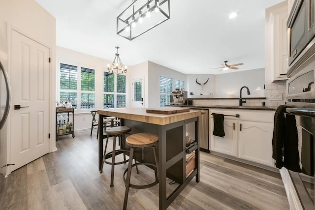 12407 Old Salt Trl, Austin, TX 78732 - kitchen with decorative backsplash, light wood-type flooring, a sink, ceiling fan with notable chandelier, and butcher block countertops