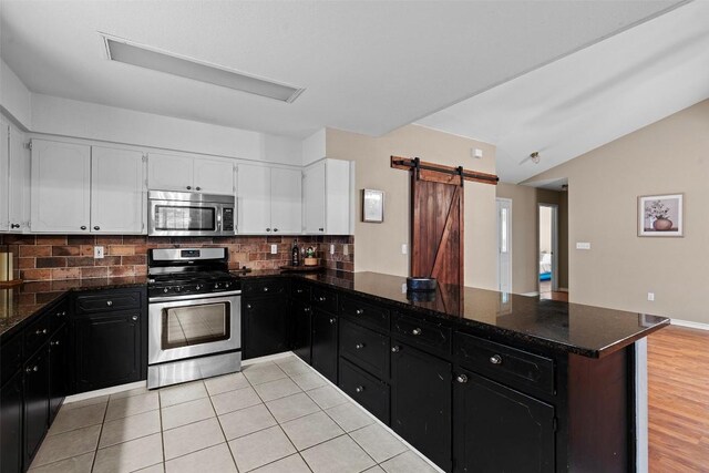 102 Vandeventer Dr, Burnet, TX 78611 - kitchen featuring appliances with stainless steel finishes, dark cabinets, decorative backsplash, a peninsula, and vaulted ceiling