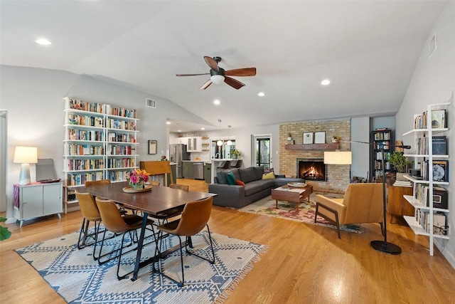 dining room featuring visible vents, lofted ceiling, a fireplace, ceiling fan, and light wood-style flooring
