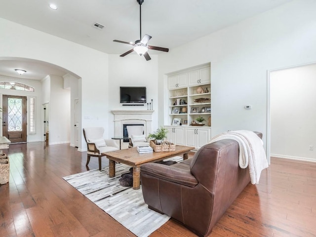 living room with ceiling fan, a fireplace, wood-type flooring, arched walkways, and visible vents