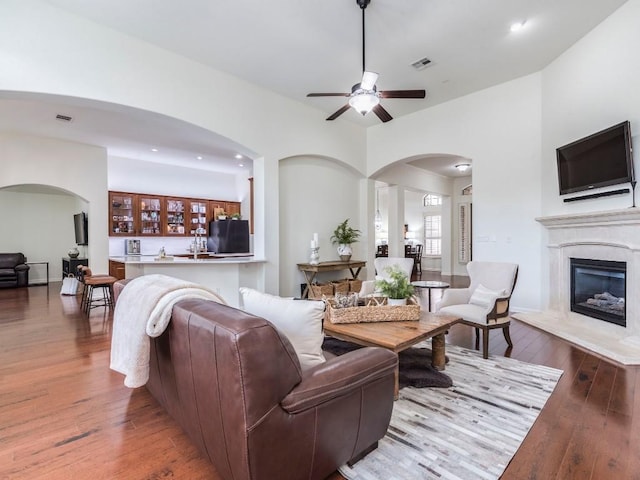 living area featuring ceiling fan, wood-type flooring, arched walkways, a glass covered fireplace, and visible vents