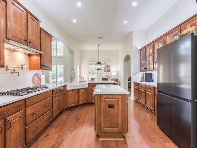 kitchen featuring a sink, arched walkways, stainless steel appliances, a peninsula, and glass insert cabinets
